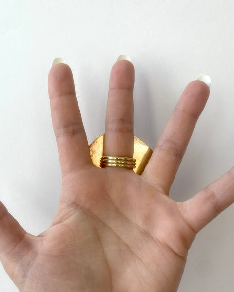 Palm of open hand with long white nails showing back of large shiny brass ring between the fingers 