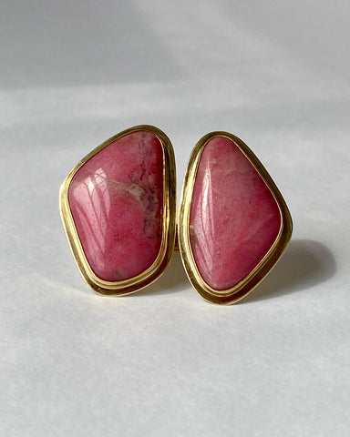 Front view of large brass statement ring featuring two pieces of pink abstract-shaped rhodonite stones with shiny brass borders on a white background