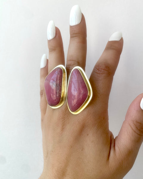 Three quarters view of large brass statement ring featuring two abstract shaped pieces of pink rhodonite stone with shiny brass borders shown on hand with long white nails