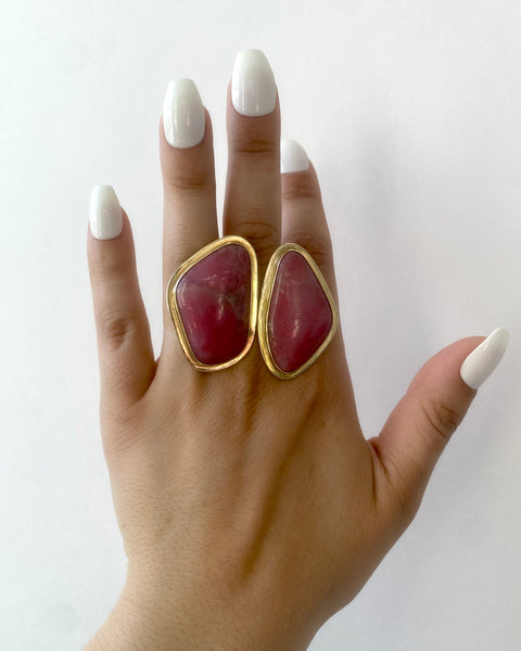 Large brass statement ring featuring two abstract shaped pieces of pink rhodonite stone with shiny brass borders shown on hand with long white nails