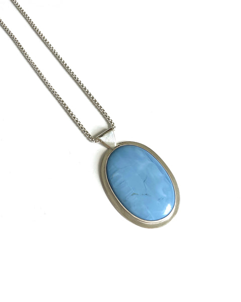  Long silver necklace with large oval-shaped smooth matte blue opal stone set in shiny sterling silver with a silver boarder and bail connection to 30 inch shiny silver box chain shown partially as a product shot on a white background